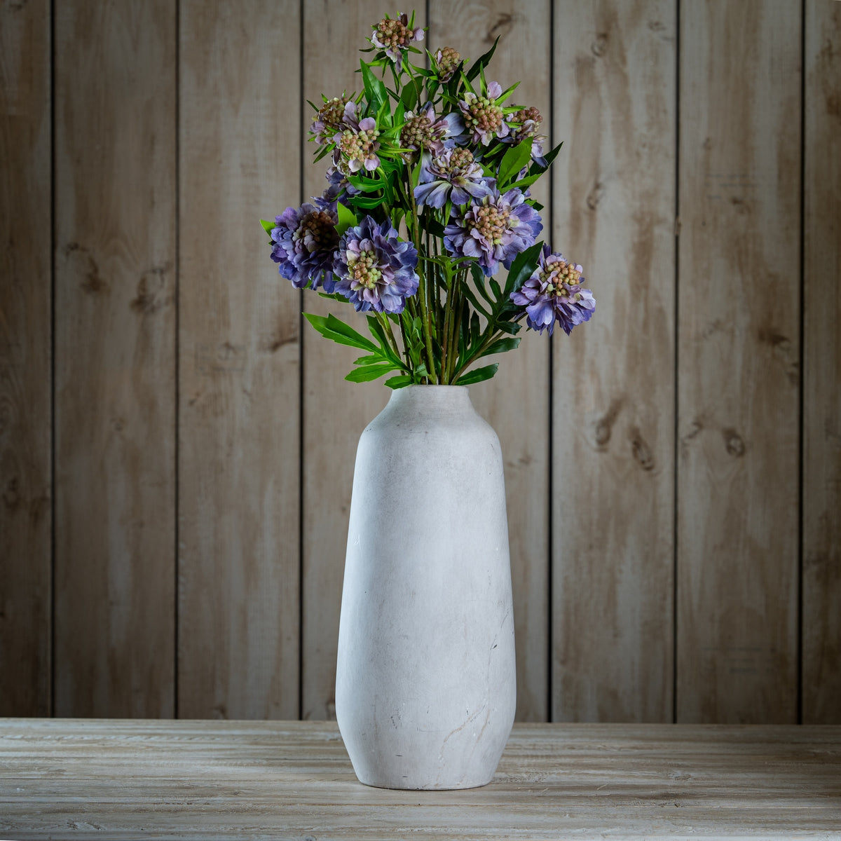 White vase with purple flowers against a wooden background